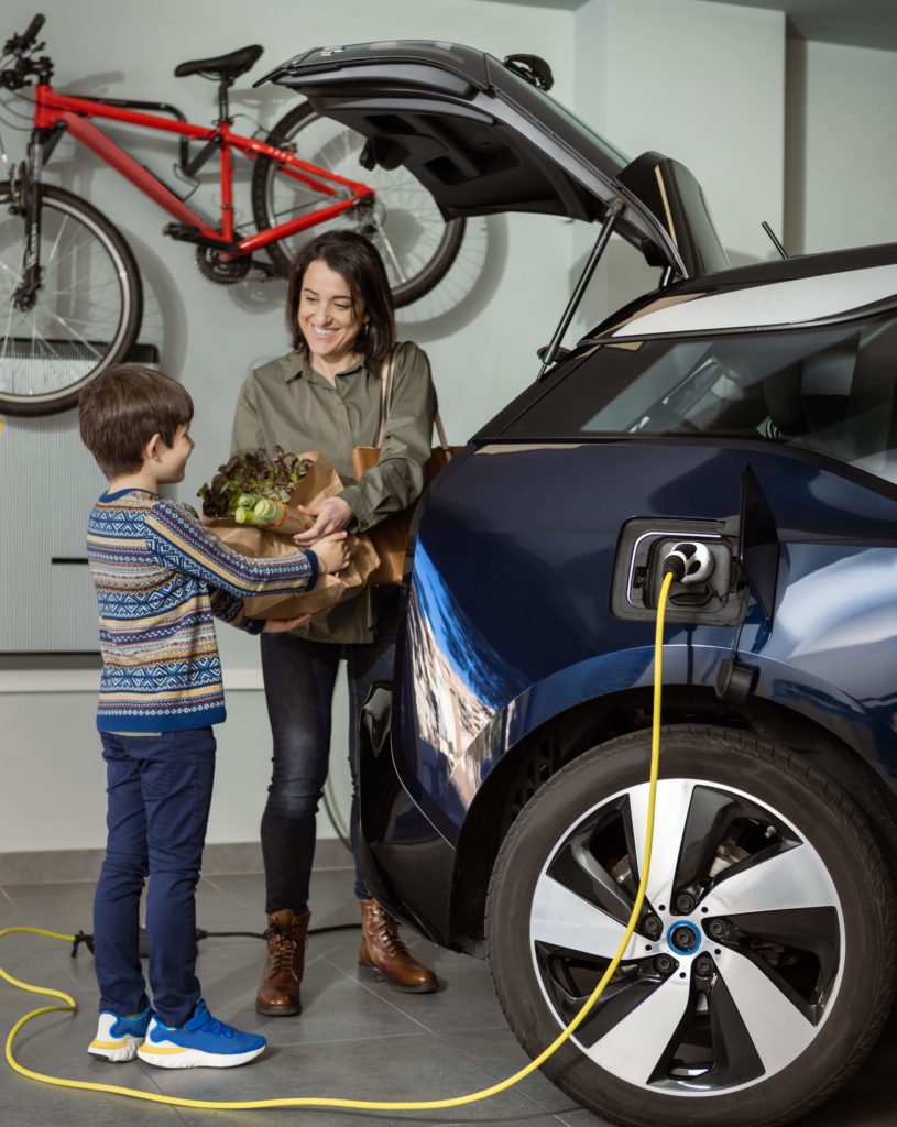 Woman and boy pick up the groceries while electric car is charging at home inside the garage